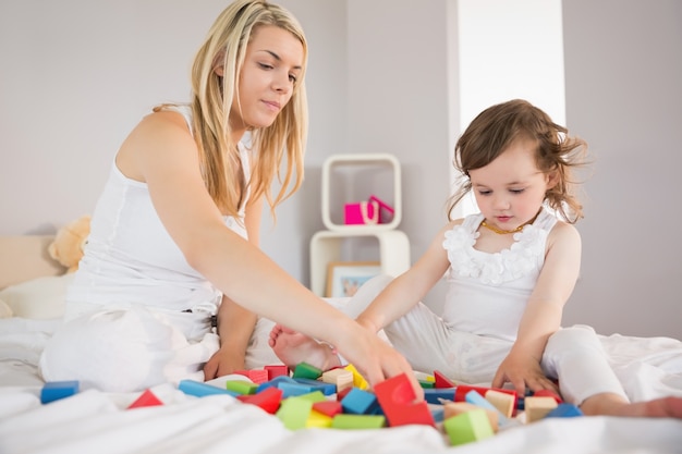 Mutter und Tochter, die mit Bausteinen auf Bett spielen