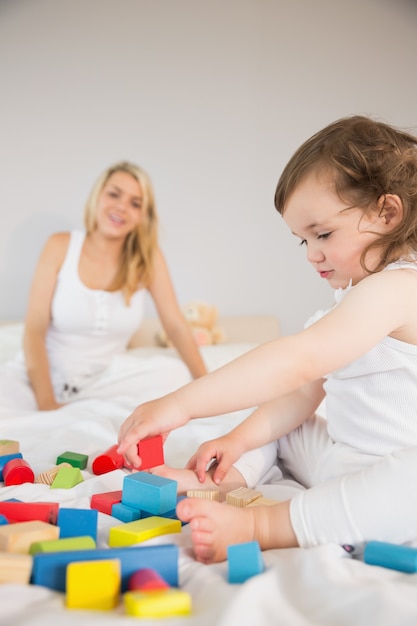 Mutter und Tochter, die mit Bausteinen auf Bett spielen