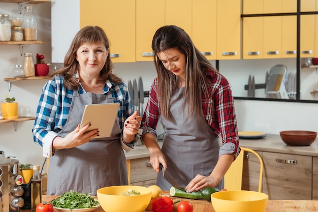 Mutter und Tochter, die Tablette beim Kochen in der Küche verwenden