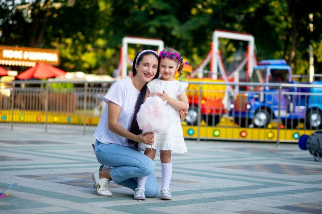 Mutter und Tochter essen im Sommer Zuckerwatte und lächeln vor Glück in einem Vergnügungspark