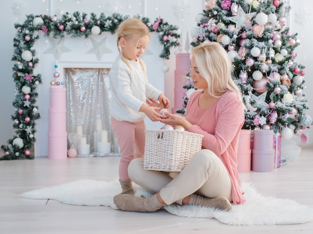 Mutter und Tochter haben Spaß auf dem Hintergrund des Weihnachtsbaums, der für den Feiertag sich vorbereitet