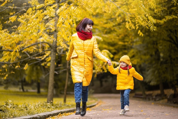 Mutter und Tochter haben Spaß beim Laufen und Lachen im Herbstpark zwischen den schönen gelben Bäumen. Glückliche Familie genießt die gemeinsame Zeit