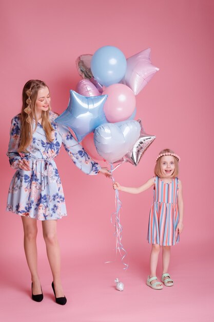 Mutter und Tochter halten ein paar Luftballons gegen eine rosa Oberfläche. Familie