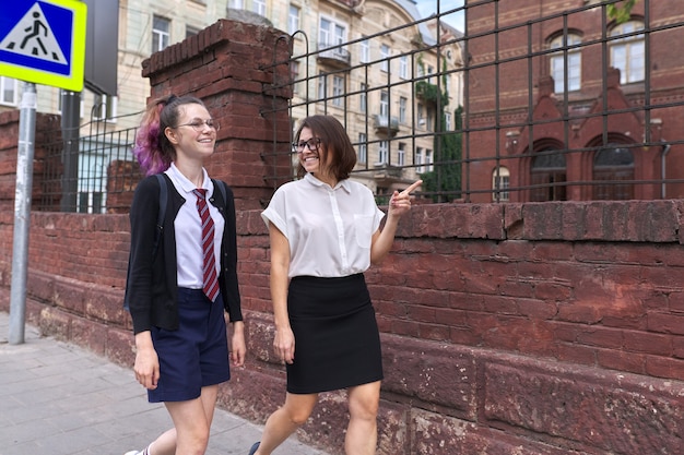 Mutter und Tochter im Teenageralter gehen zusammen auf der Stadtstraße. Sprechende Mutter und Studentin, Eltern und Kind diskutieren über Schule, Studium