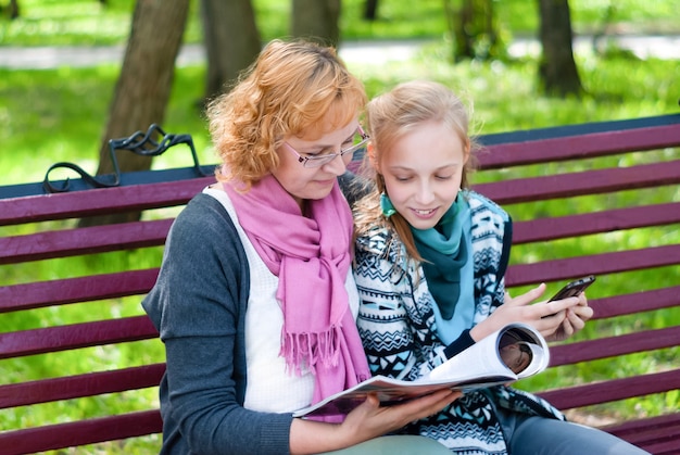 Mutter und Tochter im Teenageralter lesen eine elektronische Papierversion und eine mobile elektronische Version einer Zeitschrift