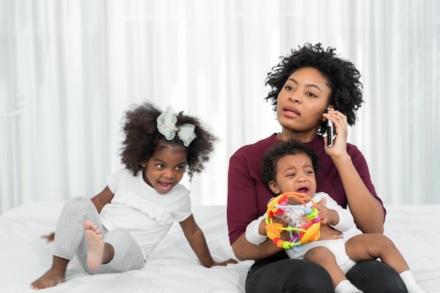 Foto mutter und tochter im wohnzimmer eine afrikanische mutter telefoniert und kümmert sich um ihre kinder, während sie von zu hause aus arbeitet