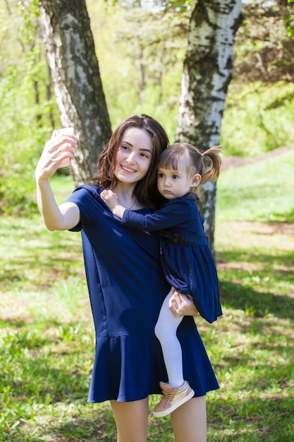 Mutter und Tochter in der gleichen Kleidung für einen Spaziergang im Park. Tochter in Mamas Armen. Die Zärtlichkeit der Mutterschaft