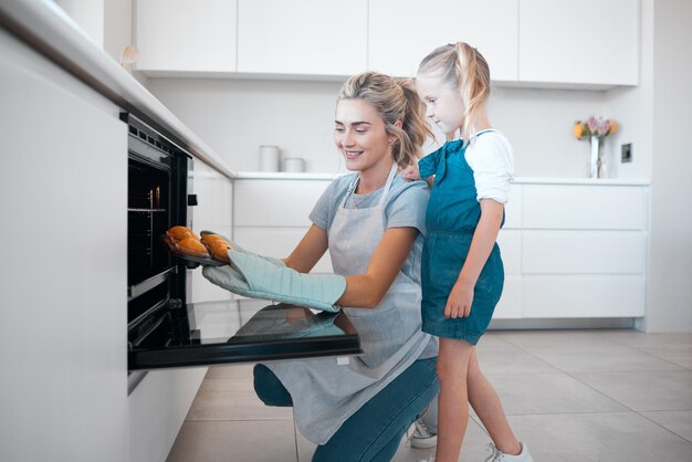 Mutter und Tochter in der Küche backen und lehren das Kind, Rezept und Muffins zu Hause zu kochen Glückliches Mädchen und Frau mit Handschuhen Lächeln und Familie mit Dessert Cupcakes und Liebe zum Essen