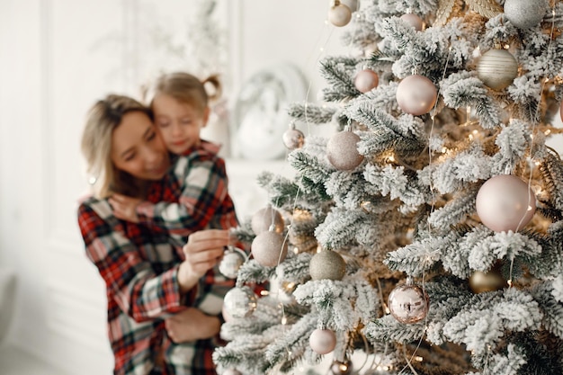 Mutter und Tochter in karierten Pyjamas umarmen sich in der Nähe des Weihnachtsbaums