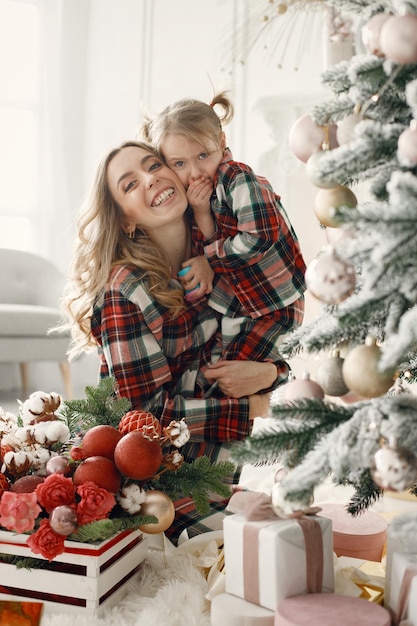 Mutter und Tochter in karierten Pyjamas umarmen sich in der Nähe des Weihnachtsbaums