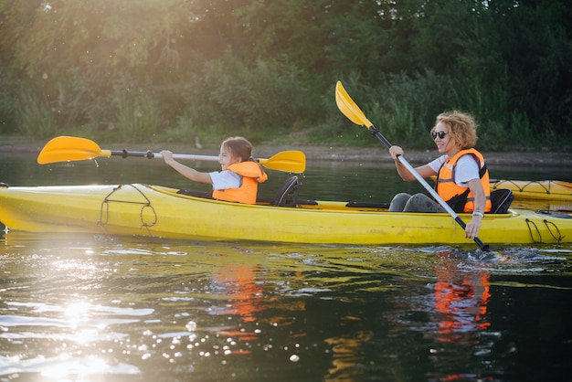 Mutter und Tochter in orangefarbenen Schwimmwesten beim Kajakfahren auf einem großen, breiten Fluss