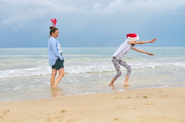 Mutter und Tochter Kind, das Spaß hat, Weihnachten an einem Strand zu feiern