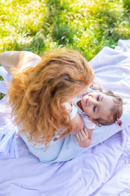 Mutter und Tochter lachen und umarmen sich auf einer Decke im Park sitzend das Konzept einer glücklichen Familie...