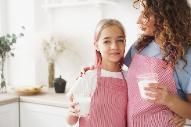 Mutter und Tochter lächeln und halten Gläser Milch in der Küche