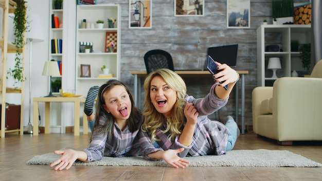 Mutter und Tochter liegen auf dem Boden und machen ein Selfie mit Smartphone.