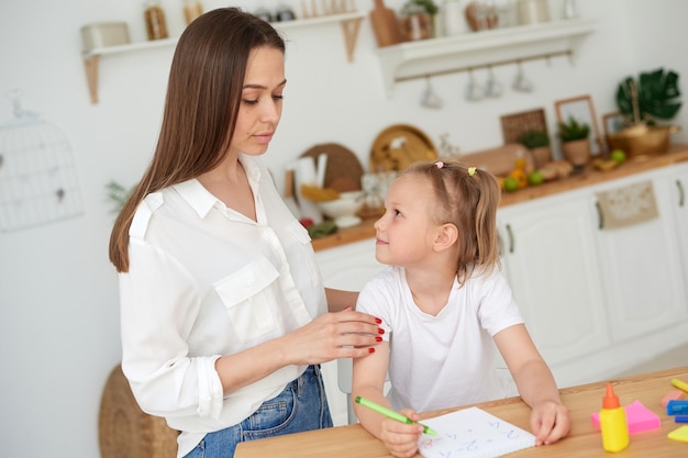 Mutter und Tochter machen Hausaufgaben. Ein kleines Mädchen erledigt unter der Aufsicht eines Tutors nachdenklich mathematische Aufgaben. Das Konzept, auf ein Kind aufzupassen und bei den Hausaufgaben zu helfen.