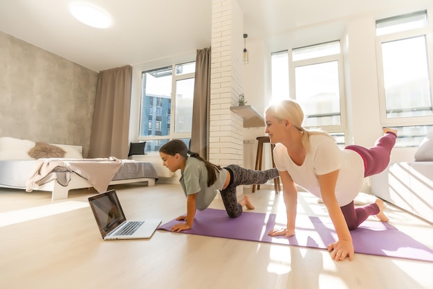 Mutter und Tochter machen Yoga-Übungen online mit Laptop zu Hause