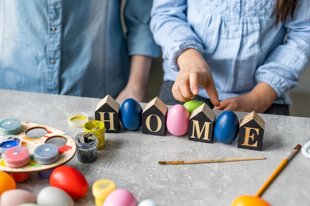 Mutter und Tochter malen Eier mit Farben. Habe Spaß. Glückliche Familie bereitet sich auf Ostern vor, hält die Inschrift nach Hause.