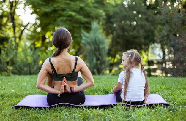 Mutter und Tochter meditieren und üben zusammen Yoga auf einer Matte im Park Mutterschaft Zeit verbringen Mutter Trainer gesundes Familienkonzept