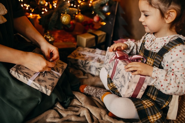 Mutter und Tochter packen Geschenke aus und sitzen neben einem Weihnachtsbaum