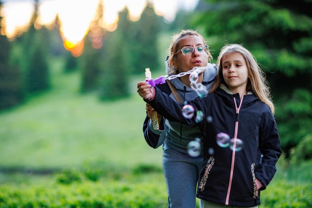 Mutter und Tochter pusten bei einem Spaziergang im Fichtenwald Seifenblasen