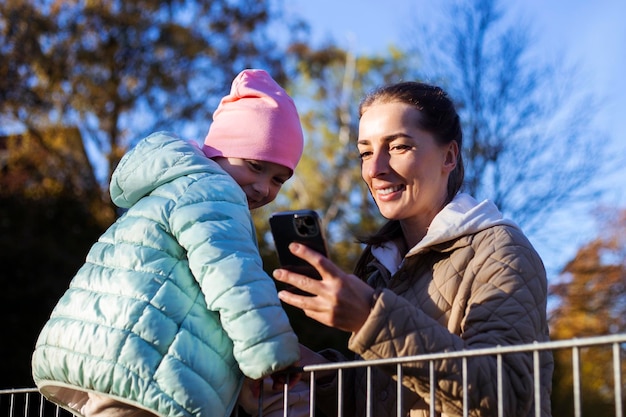 Mutter und Tochter schauen sich freudig etwas am Telefon im Park an