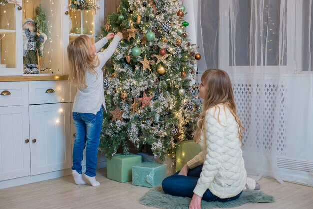 Mutter und Tochter schmücken den Weihnachtsbaumstandort süß und glücklich