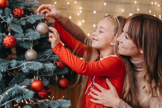 Mutter und Tochter schmücken gemeinsam den Weihnachtsbaum. Traditionelle Elternschaft.