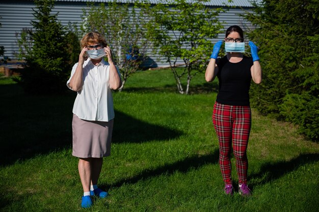 Mutter und Tochter setzen medizinische Masken auf und wahren die soziale Distanz. Zwei Frauen stehen im Park in großer Entfernung von einer Freundin, um sich gegen die Ausbreitung des Virus zu wehren