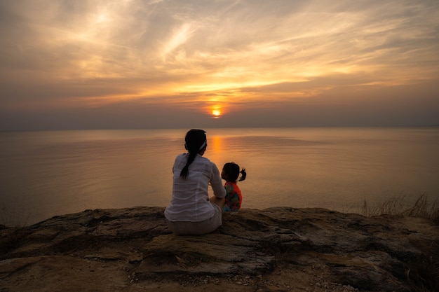Mutter und Tochter sitzen an einer Klippe gegen Sonnenuntergang scape