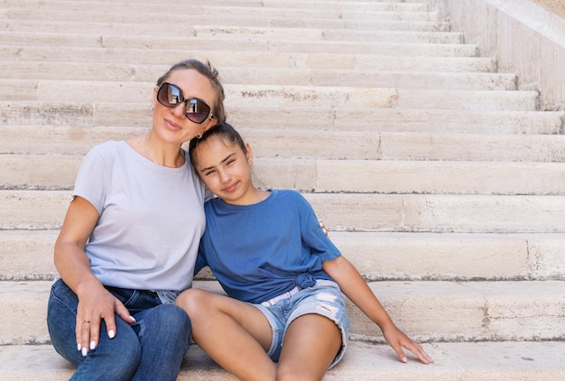 Foto mutter und tochter sitzen auf steinstufen im freien und tragen t-shirts