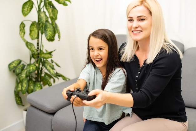 Mutter und Tochter sitzen in einem Spielzimmer, spielen Videospiele und haben Spaß.