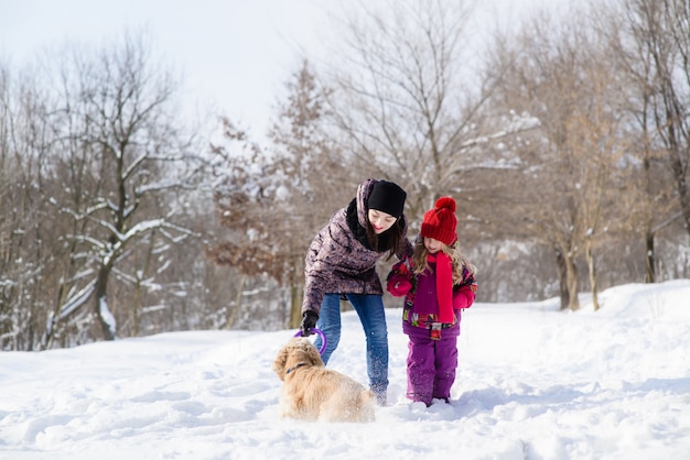 Mutter und Tochter spielen mit einem Hund im Schneewald