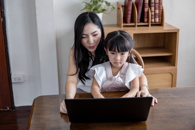 Mutter und Tochter spielen zusammen Laptop im Wohnzimmer zu Hause.