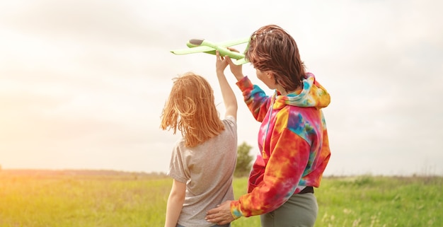 Mutter und Tochter starten Spielzeugflugzeug auf dem Feld bei Sommermädchen und -frau