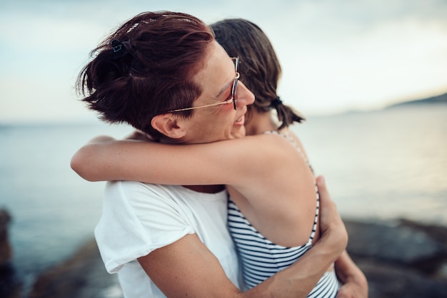 Mutter und Tochter umarmen am Strand