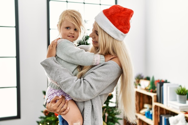 Mutter und Tochter umarmen sich und stehen zu Hause am Weihnachtsbaum