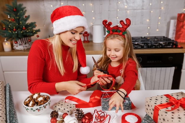 Mutter und Tochter verpacken Weihnachtsgeschenkboxen auf dem Hintergrund der dekorierten Küche