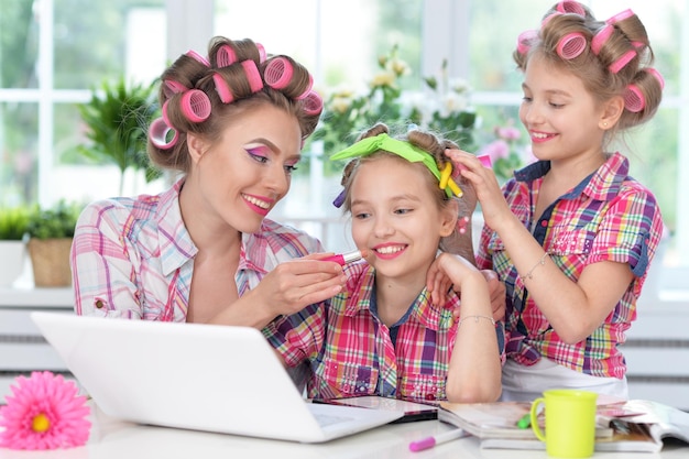 Mutter und Töchter sitzen mit Laptop am Tisch und machen Frisuren