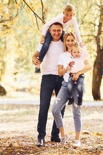 Mutter und Vater halten Kinder an den Schultern und in den Händen. Fröhliche junge Familie macht zusammen einen Spaziergang in einem Herbstpark.