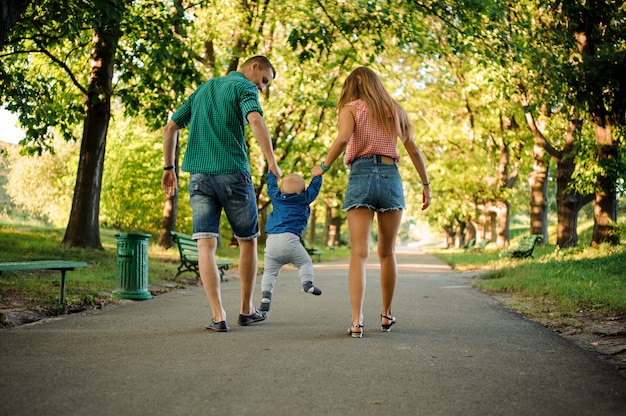 Mutter und vater mit einem baby, das in den grünen park geht