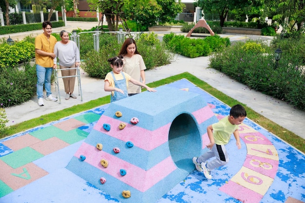 Mutter und zwei Kinder haben Spaß beim gemeinsamen Laufen, während Vater und Großmutter auf der Suche nach ihnen auf dem Spielplatz spielen