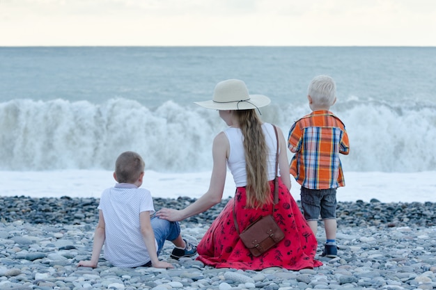 Mutter und zwei Söhne sitzen am Strand und beobachten die Wellen. Rückansicht