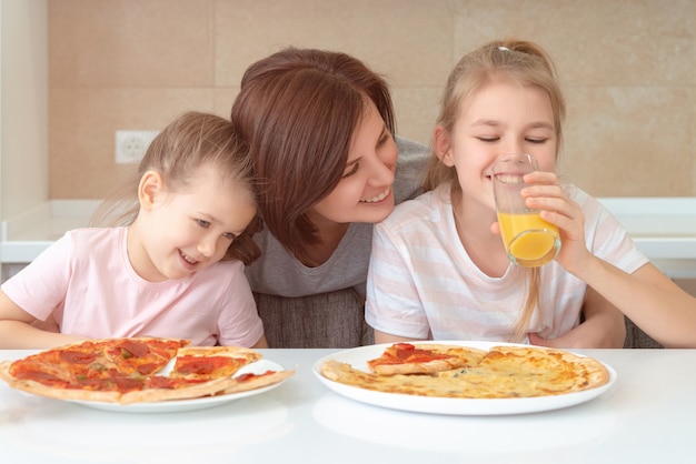 Mutter und zwei Töchter essen hausgemachte Pizza an einem Tisch in der Küche, glückliches Familienkonzept