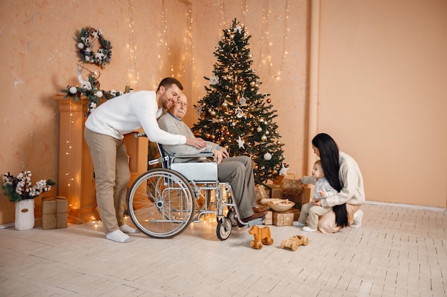 Mutter, Vater, kleiner Sohn und alter Großvater im Rollstuhl, der neben dem Weihnachtsbaum sitzt