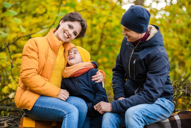 Mutter vater und kleiner sohn sitzen auf einem plaid auf einem baumstamm im herbstpark und verbringen zeit miteinander