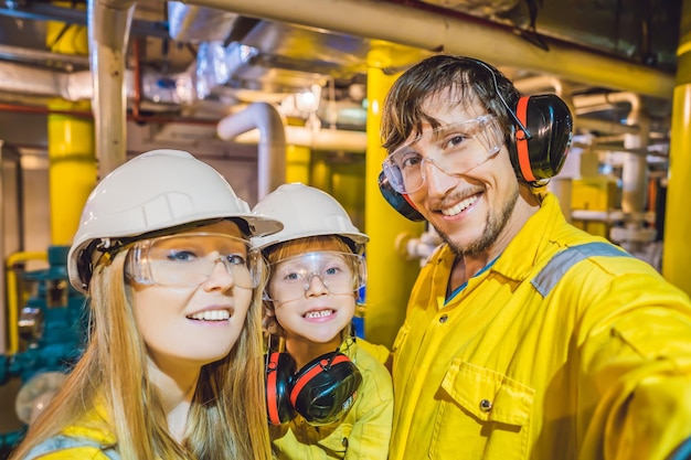 Mutter, Vater und Sohn in einer gelben Arbeitsuniform, Brille und Helm in einem industriellen Umgebungsöl