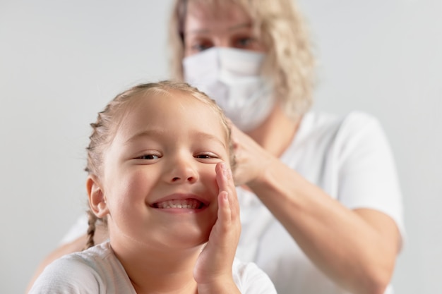 Mutter Zöpfe Zöpfe ihre Tochter in einer medizinischen Maske