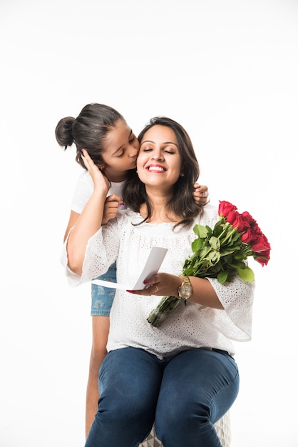 Muttertag - Indisches Mädchen und Mutter feiern den Muttertag mit Rosenblumenstrauß, Grußkarte beim Umarmen und Küssen