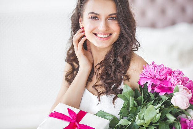 Muy bella mujer con flores y regalos en el interior